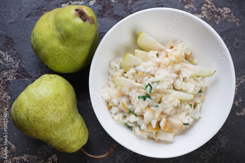 Top view of a white bowl with pear risotto on a brown stone background