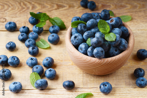 Freshly juicy blueberries with green mint leaves in light wooden bowl on rustic table. Bilberry on horizontal wooden background. Healthy eating and antioxidant nutrition concept. Top view.