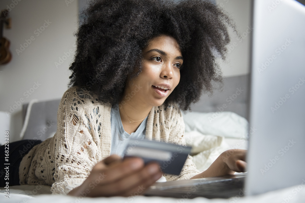 African American woman laying in bed online shopping with laptop African American woman laying in bed online shopping with laptop