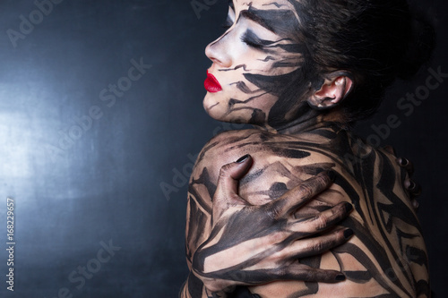 Разрисованная женщина задумчиво обнимает себя с закрытыми глазами.