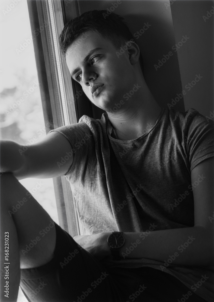 distressed teenager boy sitting on window