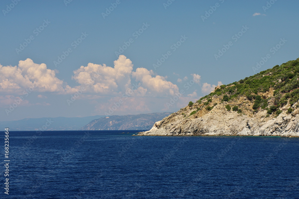 Athos peninsula, Greece. Steep edges of Athos peninsula. Blue sky with white clouds over the azure sea.