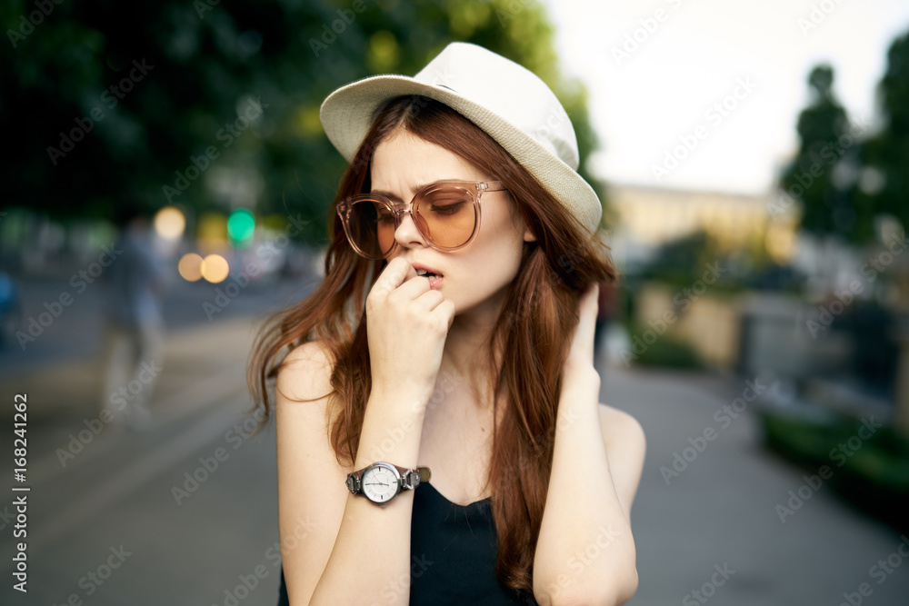 Young beautiful woman in a white hat and sunglasses outdoors in a city in summer