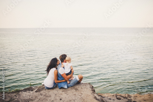 A young family of three, Mom, Dad and daughter spend one year on a high cliff looking at the sea in summer. They dressed in junior jackets and white T-shirts