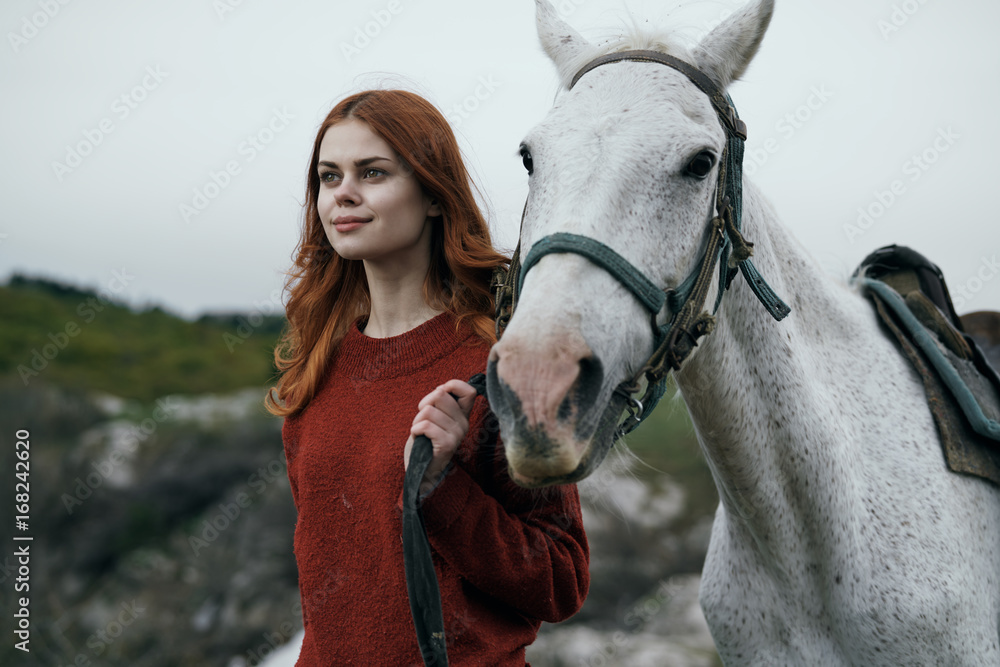 Fototapeta premium Young beautiful woman in the mountains with a white horse