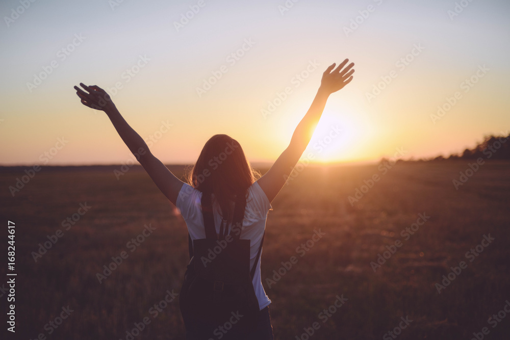 © cinana - Portrait of happy and enjoying young woman on a meadow on a sunset. Cheerful girl on sunset. Lifestyle and happiness concept. strong confidence woman open arms under the sunrise at seaside