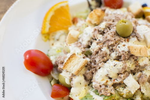 Tuna salad with lettuce, olives, and tomatoes. Orange decoration on a white plate.
