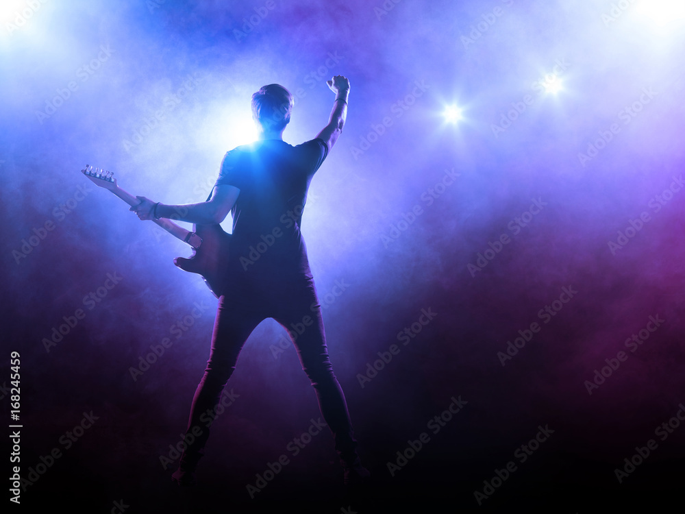 Silhouette of guitar player on stage on blue background with smoke and spotlights	
