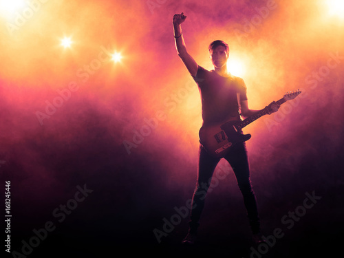 Silhouette of guitarist on stage on smoky background with spotlights	