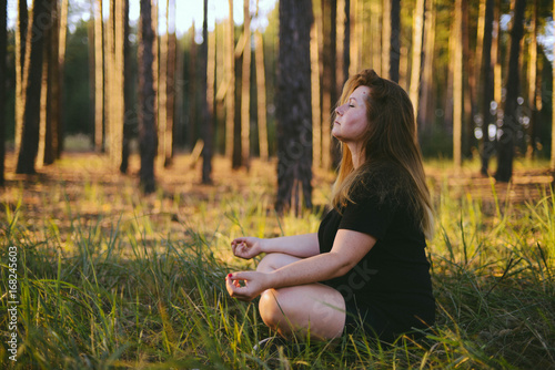 Middle aged woman sitting in lotus position in forest. her eyes are closed. Middle-aged woman in her 40s meditating for exercise outdoors