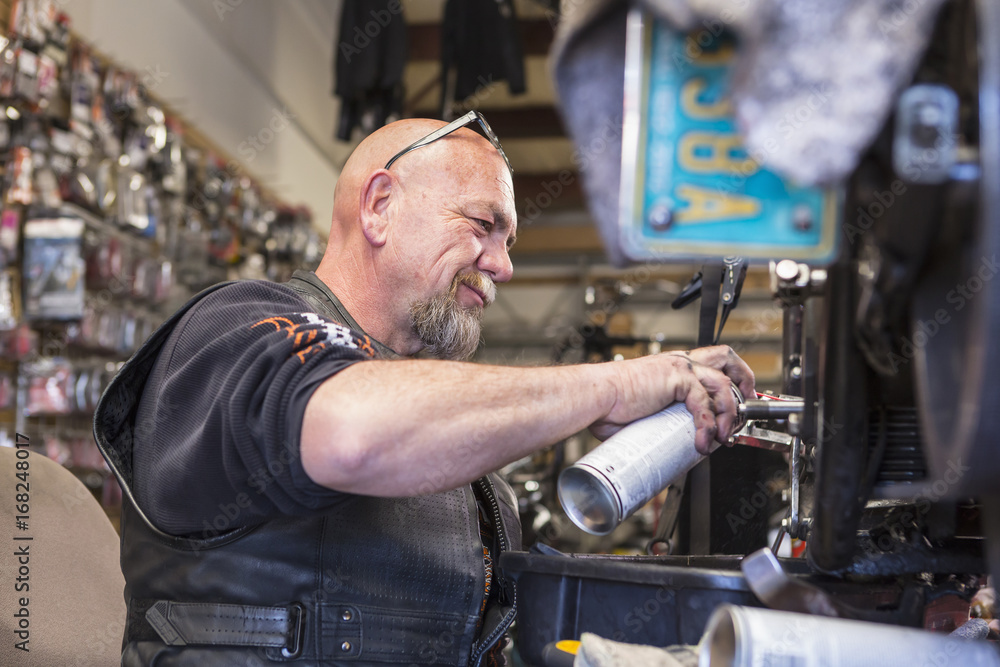 Caucasian man spraying lubricant on motorcycle Caucasian man spraying lubricant on motorcycle