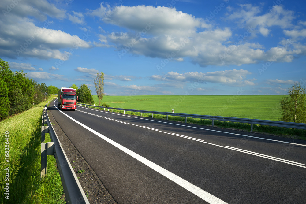 Red truck arriving on the asphalt road along a green field and alley in rural countryside Red truck arriving on the asphalt road along a green field and alley in rural countryside