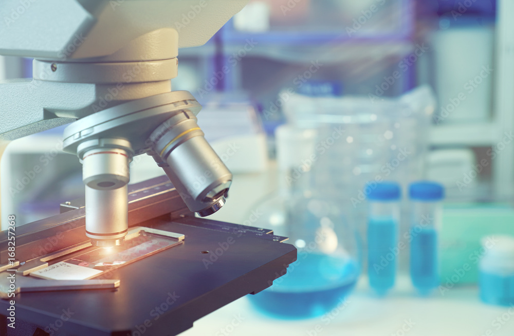 Scientific background with closeup on light microscope and blurred laboratory Scientific background with closeup on light microscope and blurred laboratory