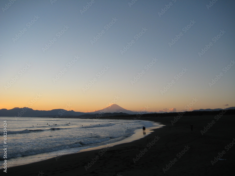 富士とサーファーのシルエットが浮かぶ波打ち際で散歩