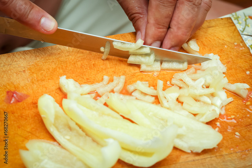 Detail of chopping yellow pepper on a cutting board in kitchen.