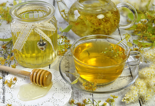 Fresh linden tea, honey in vintage jar, dipper and flowers on wooden table