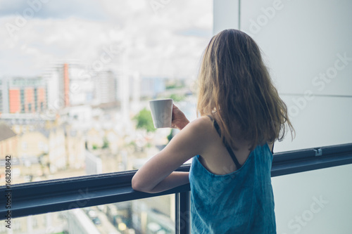 Fototapeta Woman with cup of coffee on balcony in city