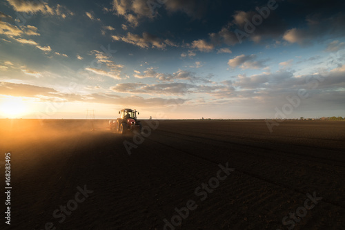 Farmer with tractor seeding - sowing crops at agricultural field in spring