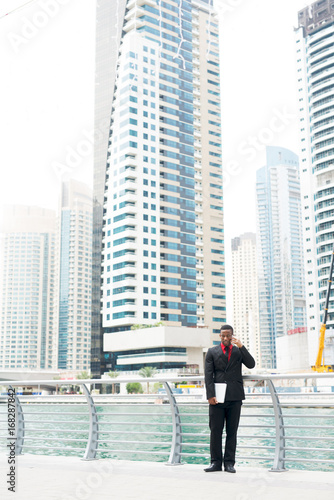 Young Afro-American businessman is standing outside in front of beautiful buildings.