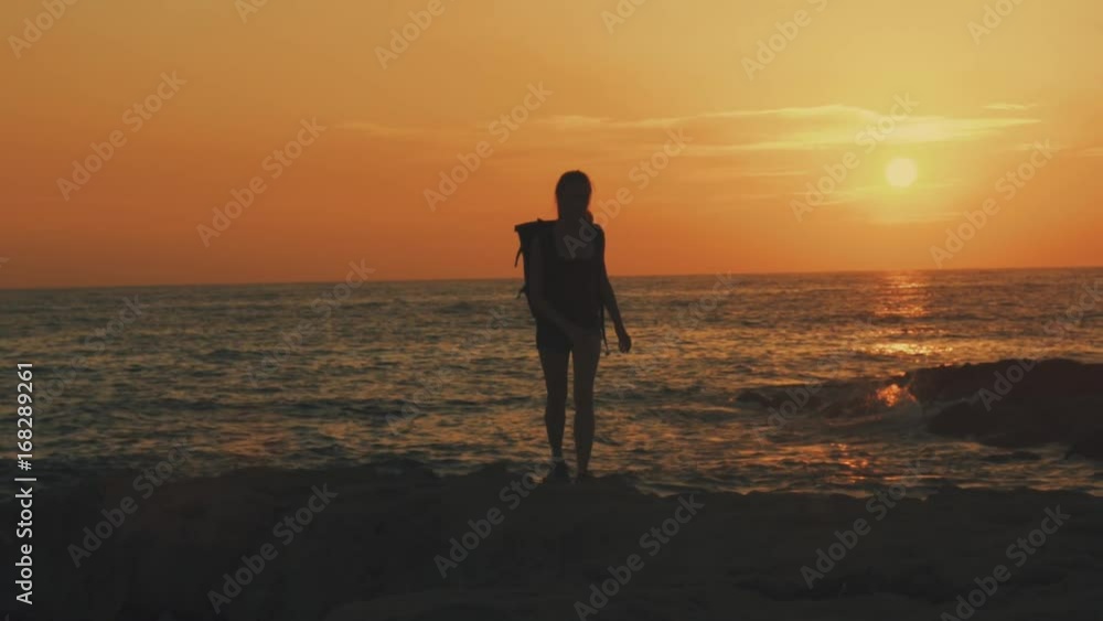 A young woman with a backpack in Cyprus is walking along the beach at sunset or sunrise against the background of orange sun and sea, sun glare, slow motion video, 100 frames per second. A young woman with a backpack in Cyprus is walking along the beach at sunset or sunrise against the background of orange sun and sea, sun glare, slow motion video, 100 frames per second.