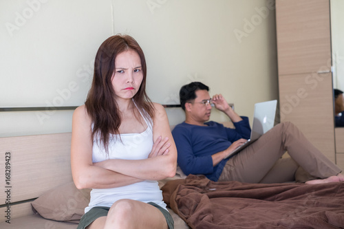 Beautiful asian women having a bad mood in the bedroom with her husband working on the background,couple having problem relationship on bed,soft focus background