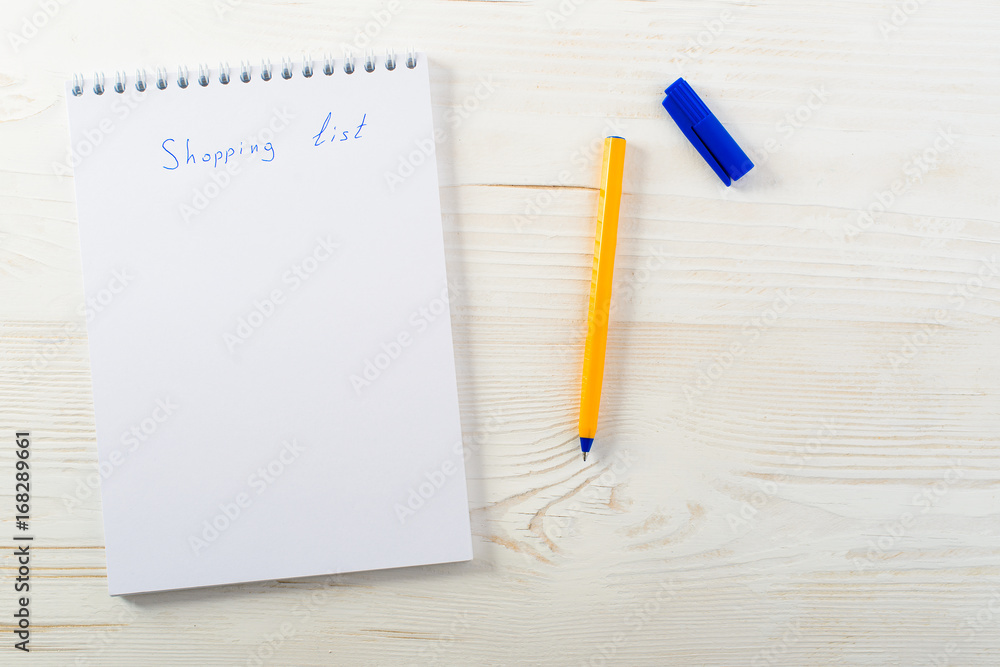 shopping list phrase in notepad with pen on light wooden table, top view, copyspace for text shopping list phrase in notepad with pen on light wooden table, top view, copyspace for text