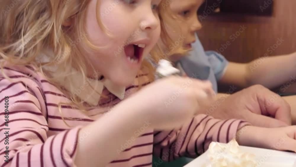 Tilt up of cute little girl eating sweet cake with whipped cream on top at cafe table Tilt up of cute little girl eating sweet cake with whipped cream on top at cafe table