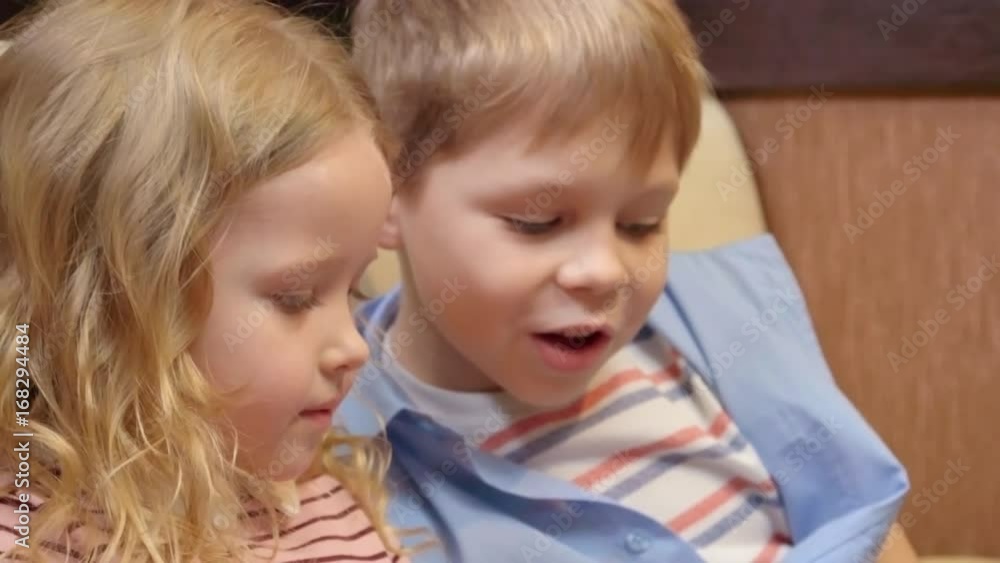 Closeup of little girl with curly blonde hair and her brother looking at something and discussing it in the cafe Closeup of little girl with curly blonde hair and her brother looking at something and discussing it in the cafe