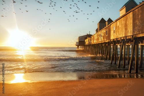 Early morning by the ocean. Wooden old pier leaving in the sea with wooden buildings. Birds flying in the sky. USA. Portland. Maine. 