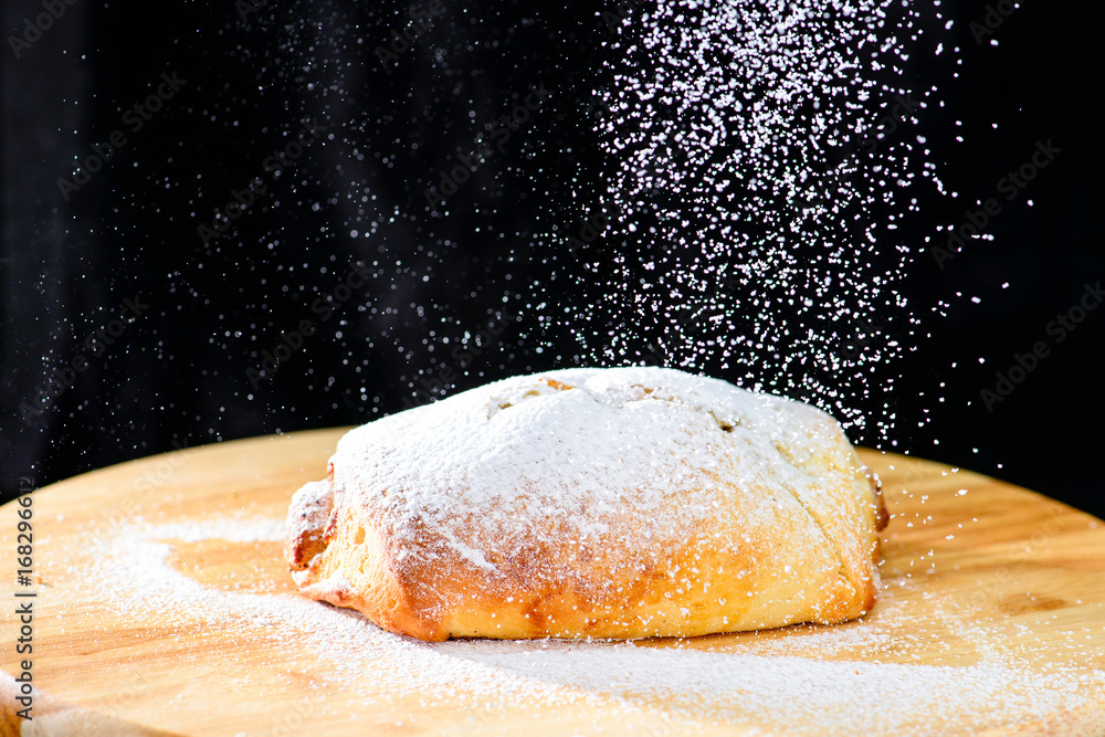 freshly baked cinnamon rolls sprinkled with powdered sugar on wooden board, dark background. Bakery goods freshly baked cinnamon rolls sprinkled with powdered sugar on wooden board, dark background. Bakery goods