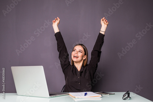 Young happy attractive woman at modern office desk, with laptop feeling with raised hands of celebreting cheerful good morning news, working toward success and reached it photo