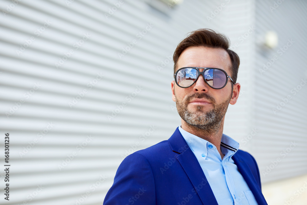 Portrait of handsome middle-aged businessman in sunglasses looking away in outside urban setting Portrait of handsome middle-aged businessman in sunglasses looking away in outside urban setting