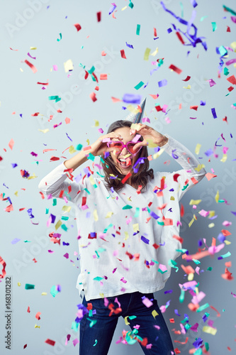 Attractive young woman raising arms and laughing celebrating birthday with confetti around her