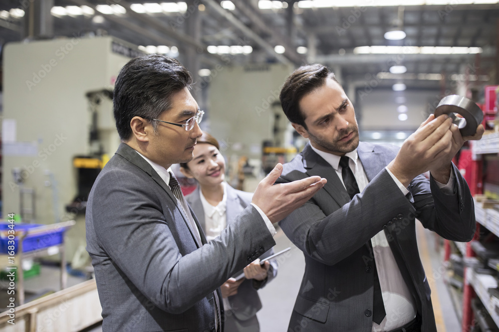 Business people checking machine parts in the factory Business people checking machine parts in the factory
