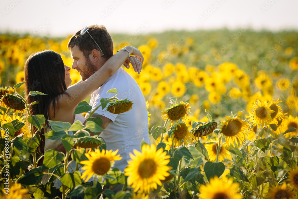 Beautiful and young woman hugging her husband, the couple is in the flowering field of sunflowers, lovers are happy on a sunny summer day Beautiful and young woman hugging her husband, the couple is in the flowering field of sunflowers, lovers are happy on a sunny summer day