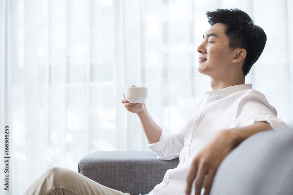 Cheerful young man drinking coffee at home