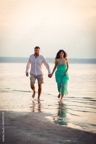 Husband and wife running along the river bank barefoot, a woman holding a dress