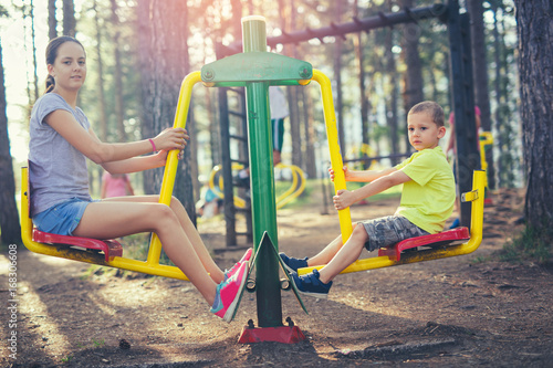 Brother and sister are exercise outdoors in a park with exercise machines