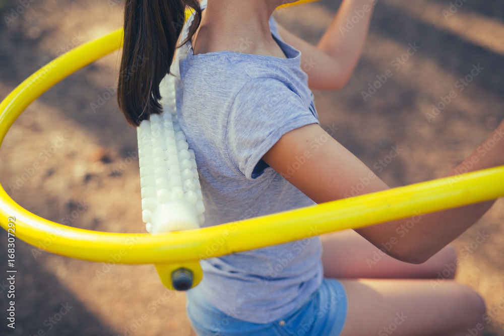 Fototapeta premium Young smiling teenage girl does exercises at massager simulator in park