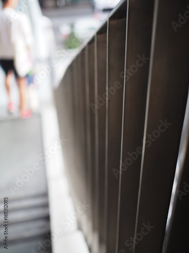 Perspective close up stacked iron ladder fence, with blurred pedestrian legs background