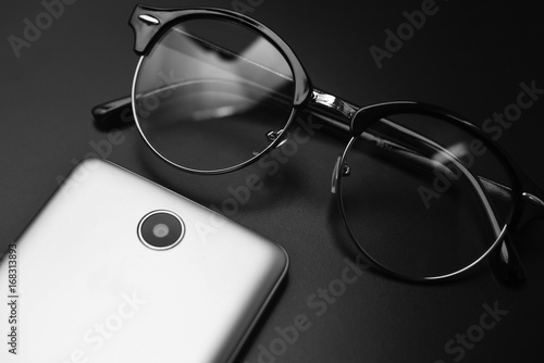 Smartphone And Black Eyeglasses Over Black Background