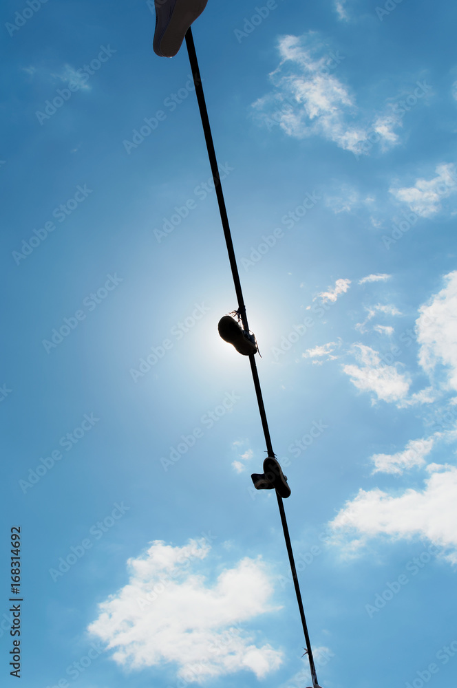 Several pairs of sneakers hanging on a rope against the blue sky. One of the shoes covers the sun.