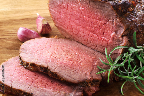 Baked meat, garlic and rosemary on a wooden background. Roast beef.