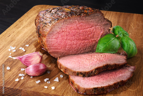 Photography Baked meat, garlic and basil on a wooden background. Roast beef.