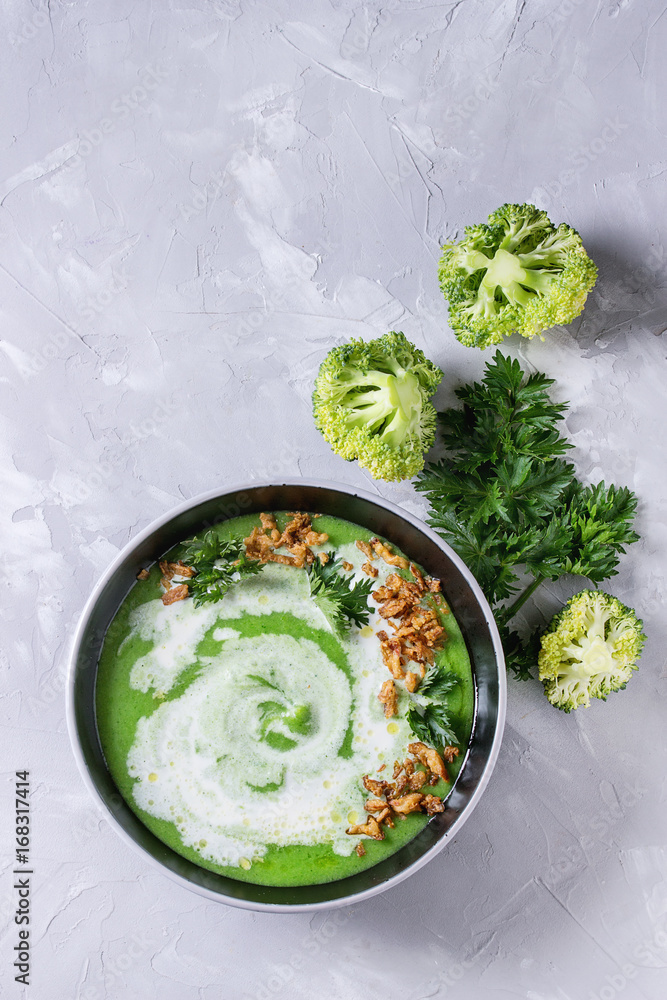 Vegetarian broccoli cream soup served in black bowl with cream, fried onion, fresh parsley and broccoli over over gray concrete background. Top view with space. Healthy eating. Vegetarian broccoli cream soup served in black bowl with cream, fried onion, fresh parsley and broccoli over over gray concrete background. Top view with space. Healthy eating.