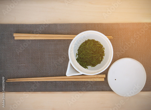 Pot of green tea and 2 pairs of wood chopstocks on grey clothe mat on wood table prepared for tea leaves eating dish. photo