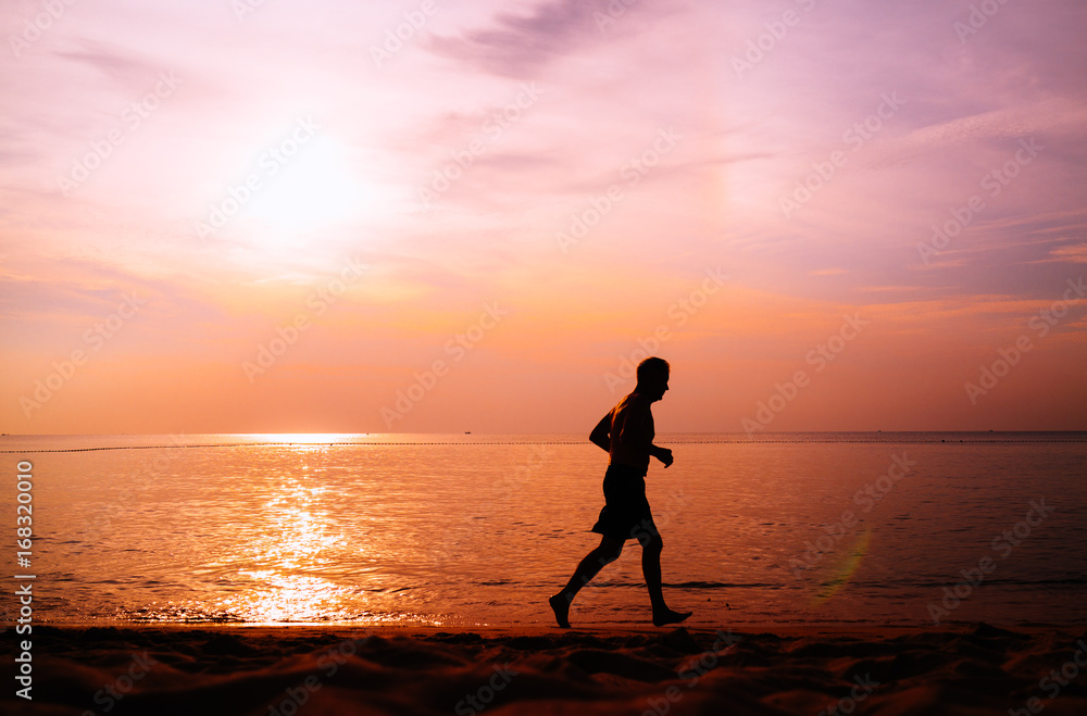 Silhouette of man jogging on the beach at sunset