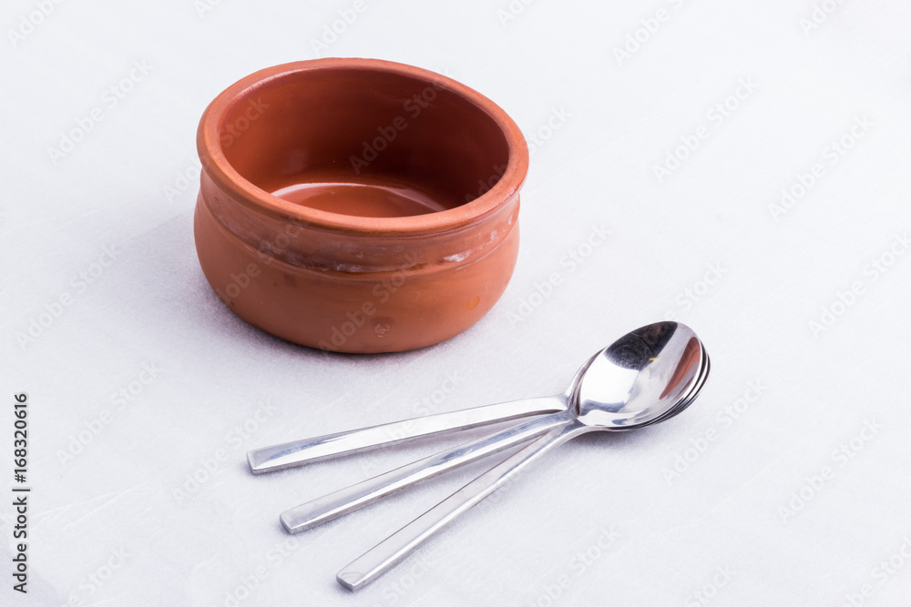 A brown bowl made out of clay and three little spoons A brown bowl made out of clay and three little spoons