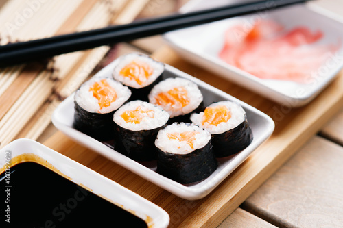 Fotografie, Obraz Sushi rolls with salmon, chopsticks and dishes with soy sauce and ginger