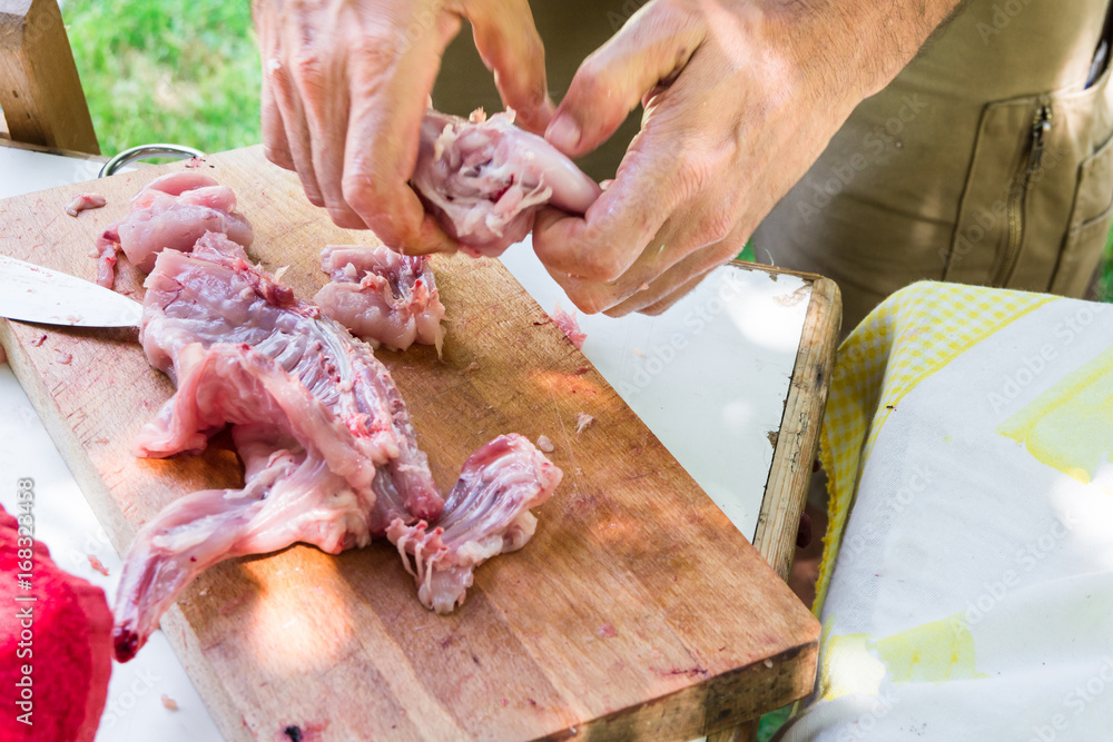 Man's hands cutting and disjointing raw rabbit meat. Preparing ingredients for cooking paella jambalaya, barbecue. Outdoor picnic, weekend, summer. Lifestyle.